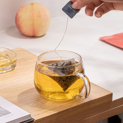 A glass cup of brewed peach oolong tea with the tea bag on a wooden surface with a peach in the background