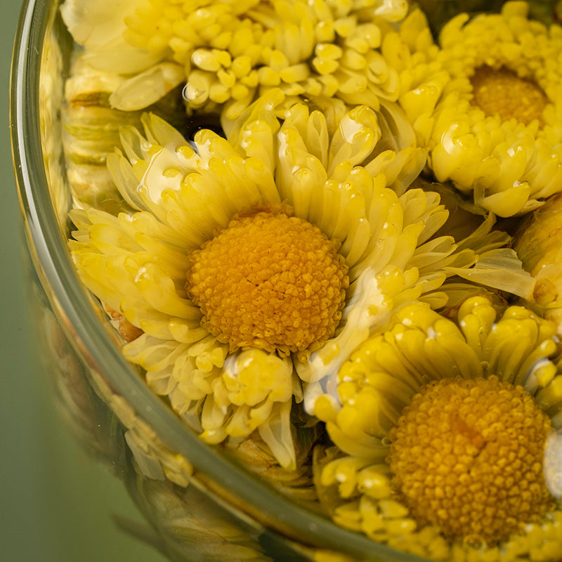 Close-up of yellow chrysanthemum flowers in a glass jar with a blurred green background